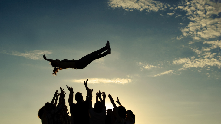 Een groep mensen vangt gezamenlijk een vrouw op die uit de lucht komt vallen