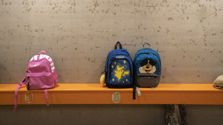 3 schooltassen staan op een houten bank in de gang van een school