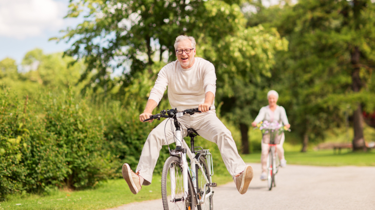 Een oudere man met fiets met de benen uitgestoken naar opzij.