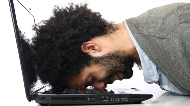 Man legt gefrustreerd zijn hoofd op zijn laptop