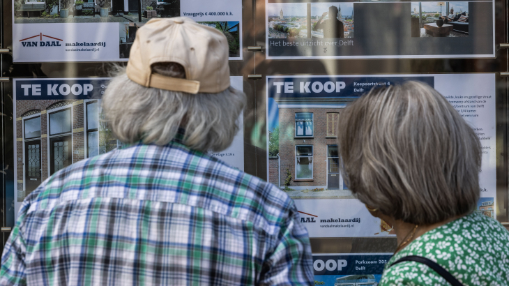 Mensen kijken naar de etalage van een Delftse makelaar.