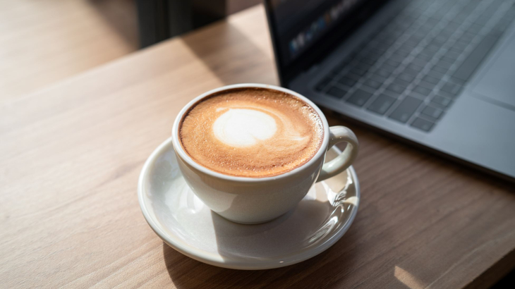 Kop Latte naast een opengeslagen laptop