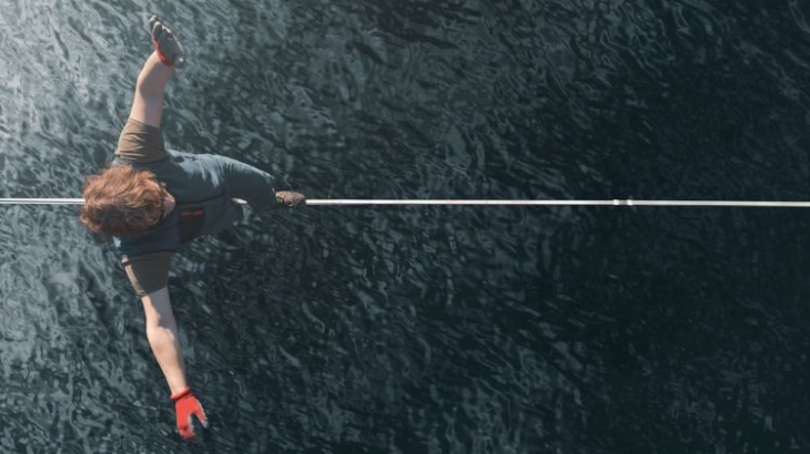 Een man balanceert op een koord over het water, van bovenaf gezien