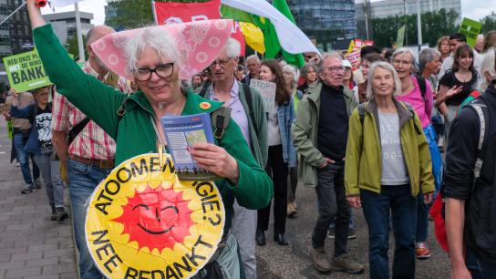 Tijdens een klimaatmars op de Zuidas in Amsterdam zwaait een vrouw met een klimaatvlag van de FNV, terwijl ze protesteert tegen kernenergie. Ook GroenLinks-PvdA liep mee.
