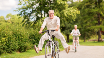 Een oudere man met fiets met de benen uitgestoken naar opzij.