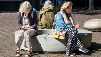 Drie vrouwen op het Domplein in Utrecht over hun smartphone gebogen