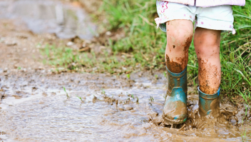 Kind in regenlaarzen stampend in een modderpoel