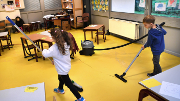 Twee kinderen helpen met het schoonmaken van een klaslokaal. Foto: Marcel van den Bergh (ANP)