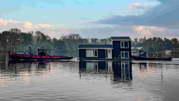 Twee sleepboten transporteren een huisje over het water van de Nieuwe Meer in Amsterdam.